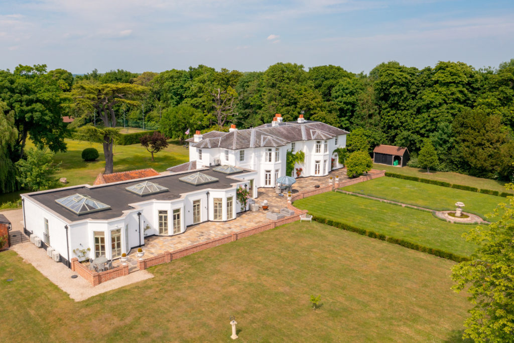 Large country manor with grey roof and surrounding gardens with a stone fountain in the centre