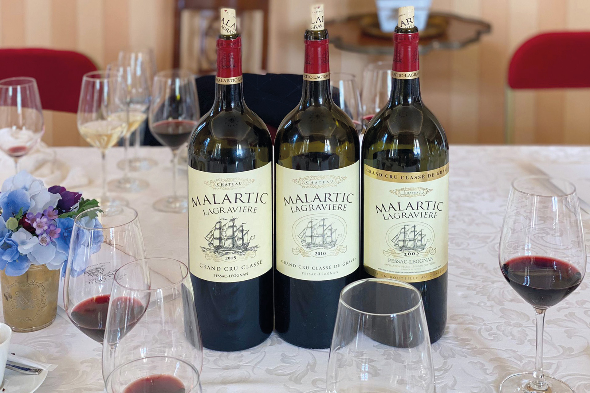 Three red wine bottles on a table, with glasses of red wine beside