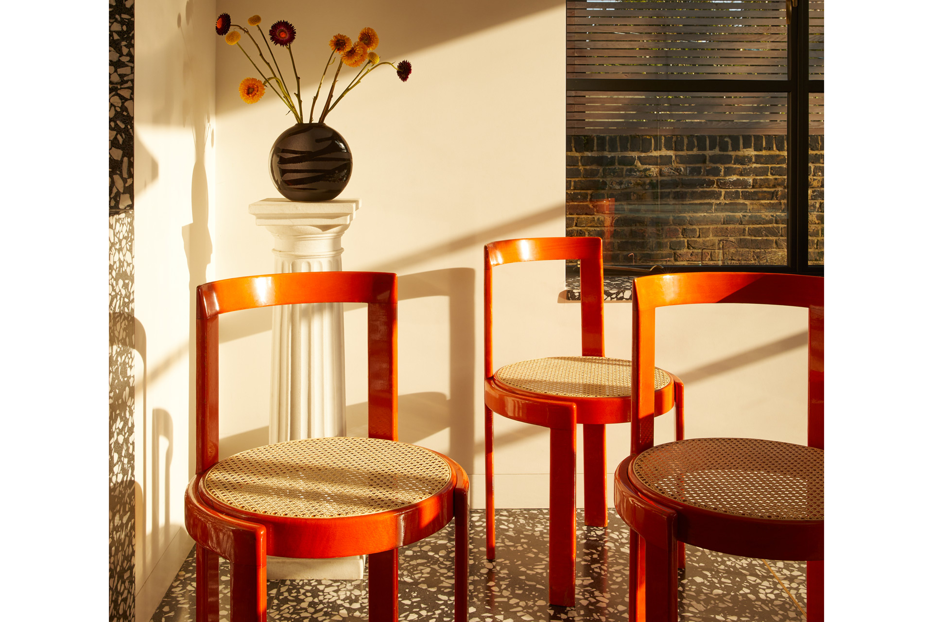 Corner with orange chairs with wicker bases and a circular vase of flowers behind