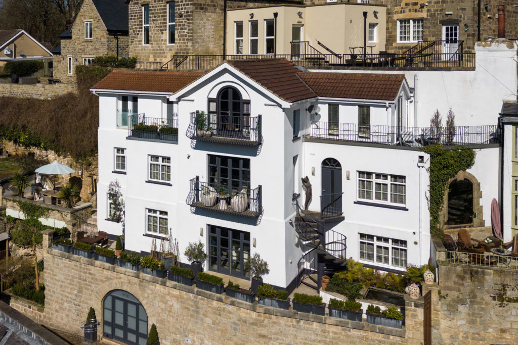 House built into the Yorkshire riverside with white exterior and black metal balconies.