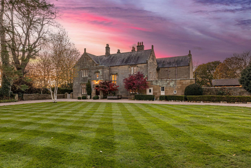 Manor house at sunset with landscaped lawns in front.