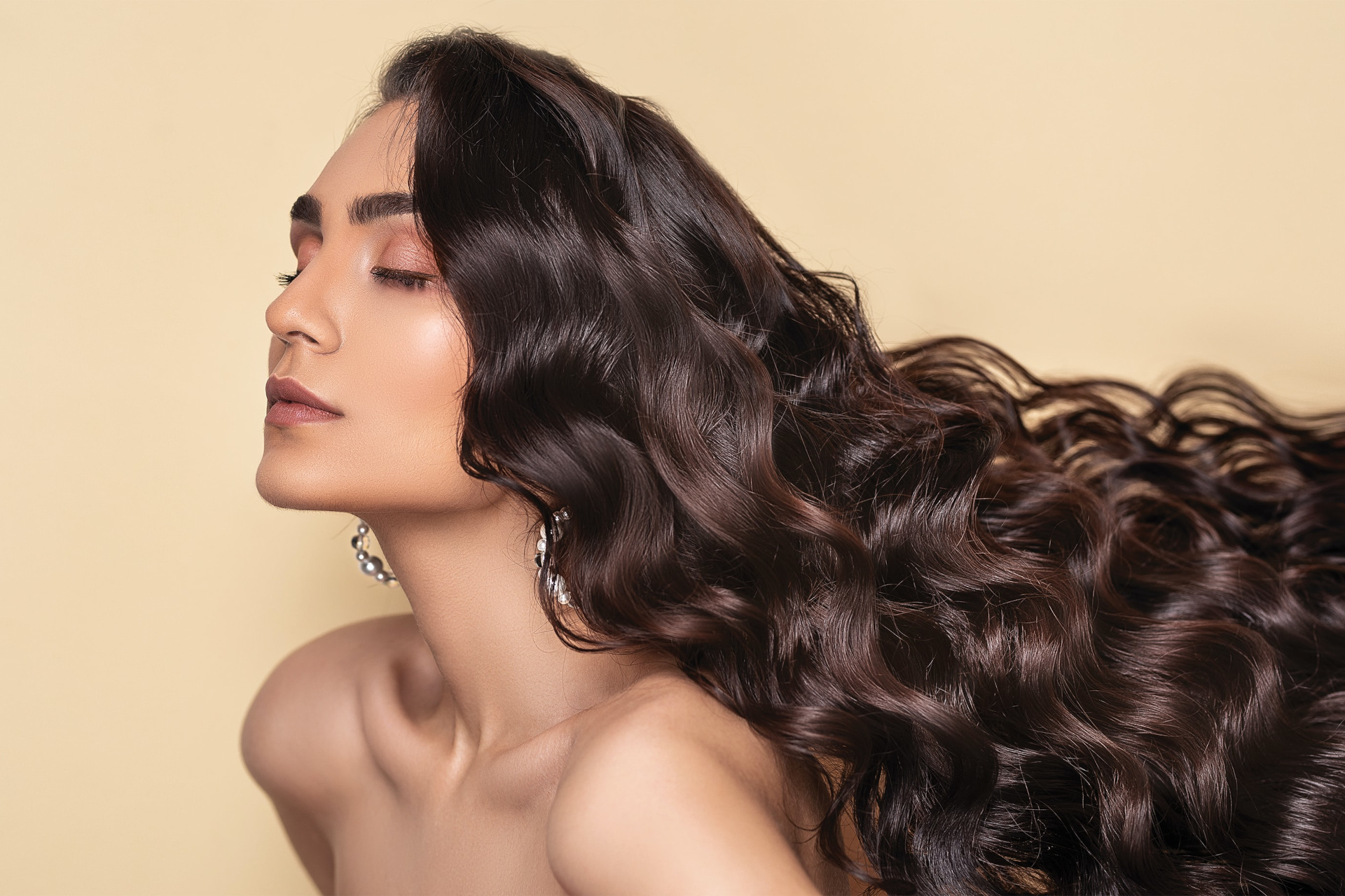 Woman with long dark hair in front of light gold background