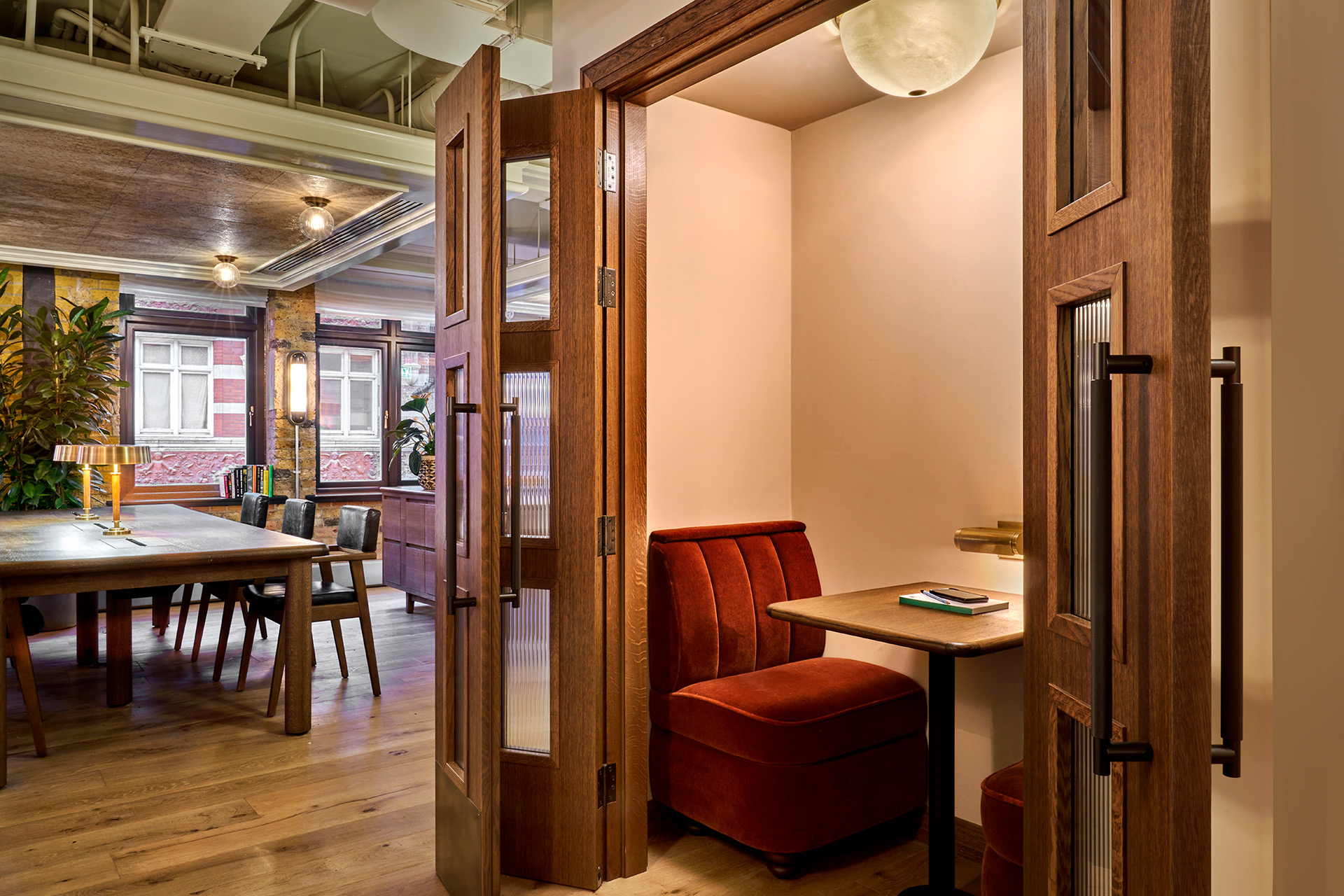 Social space with long wooden table plus a cubby hole with a small table and a rust orange velvet chair.