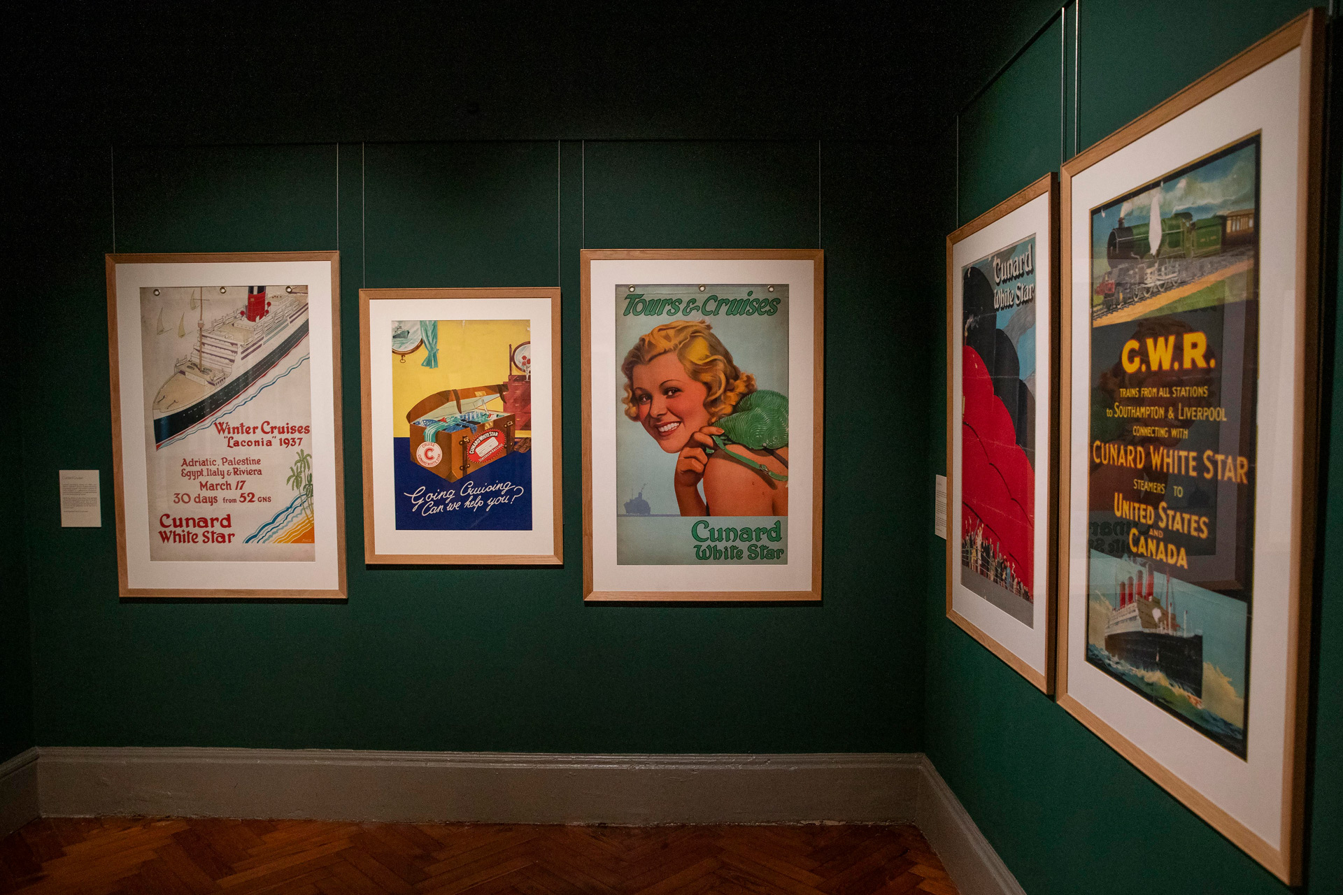 Cunard exhibition in Liverpool: old-school Cunard advert posters in frames on a dark green wall.