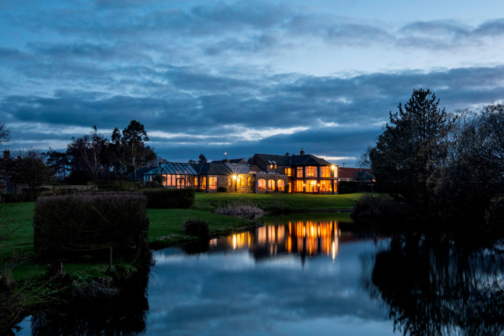 Large country estate at night with pond in foreground