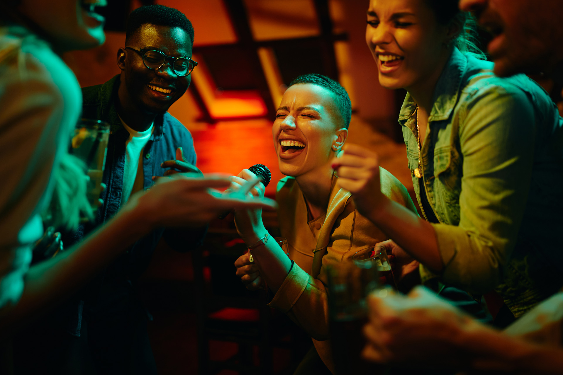 African American woman holding microphone and singing karaoke while partying with her friends at nightclub.