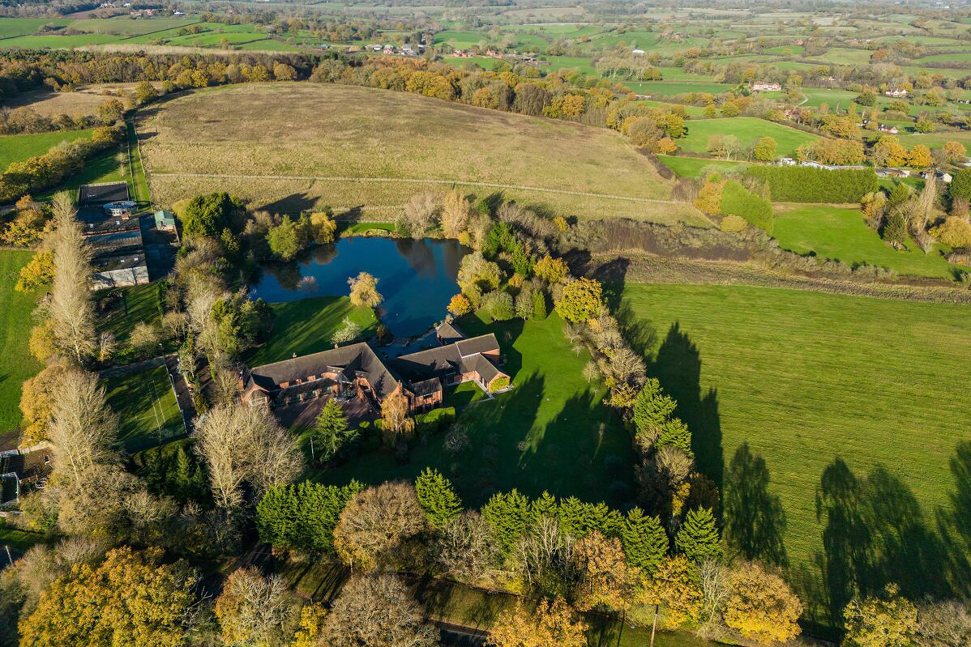 Aerial view of a large farmhouse with stables and a lake.