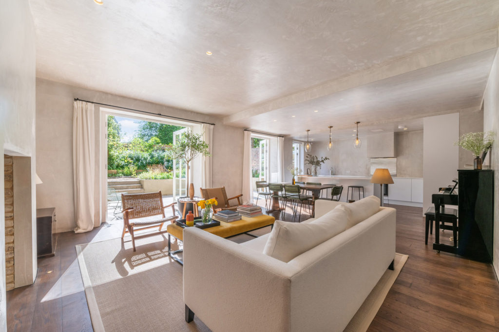 Living room with cream sofas, oak flooring and French doors leading out to a raised lawn garden.