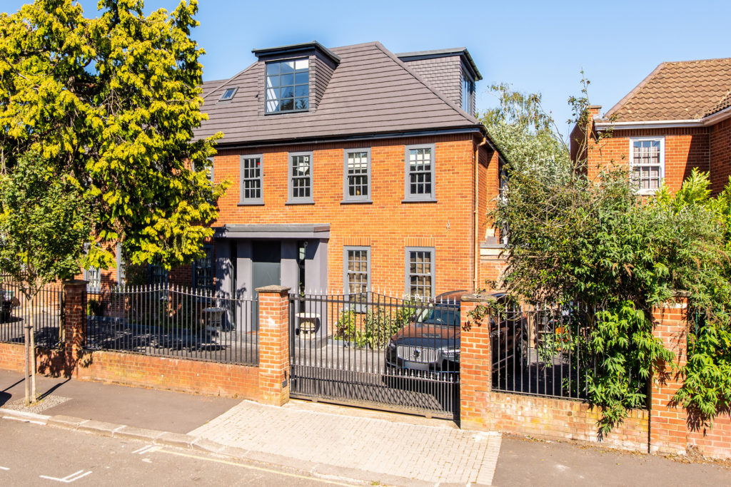Red brick house behind iron gates with grey window frames.