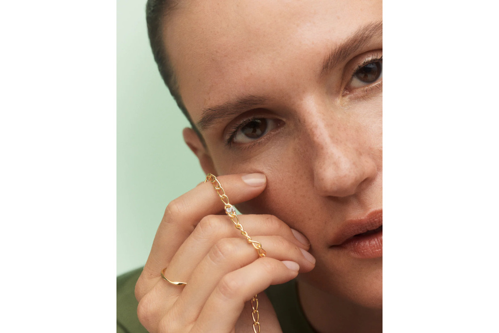 Woman holding gold bracelet with small letter on it
