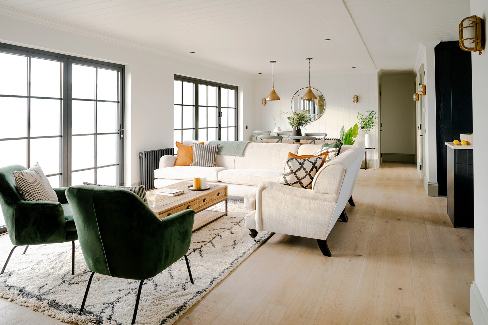 Large modern living room with cream sofas and dark green velvet chairs.