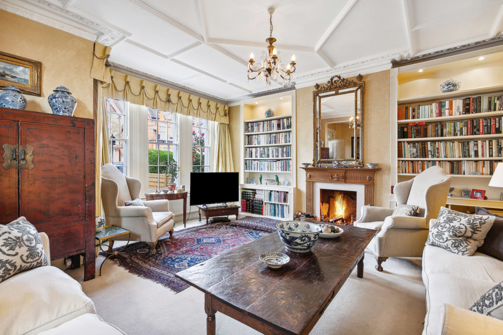 Drawing room with ceiling cornicing, bookshelves, cream sofas and dark wooden coffee table.