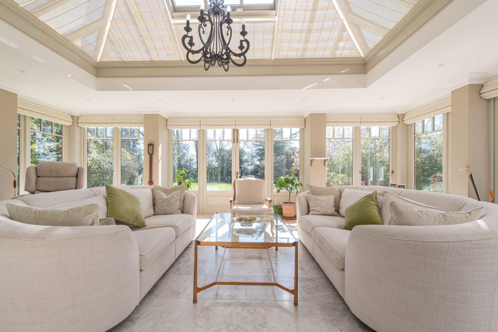 Orangery with vaulted glass ceiling, French doors and cream sofas with rounded arms.