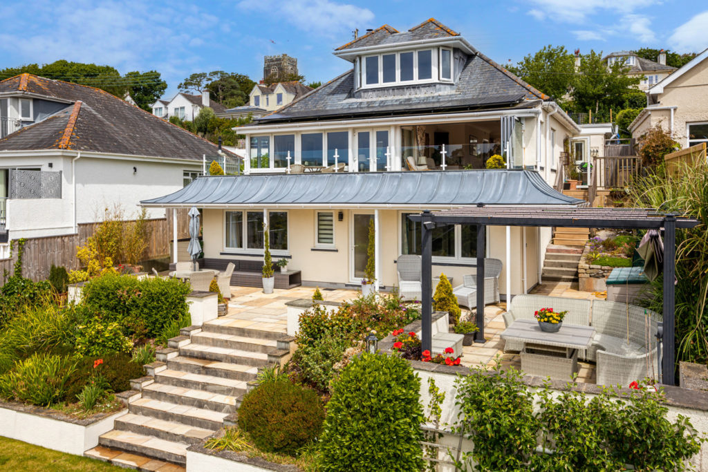 Waterfront Devon property set on an elevated area with shrubs in front.