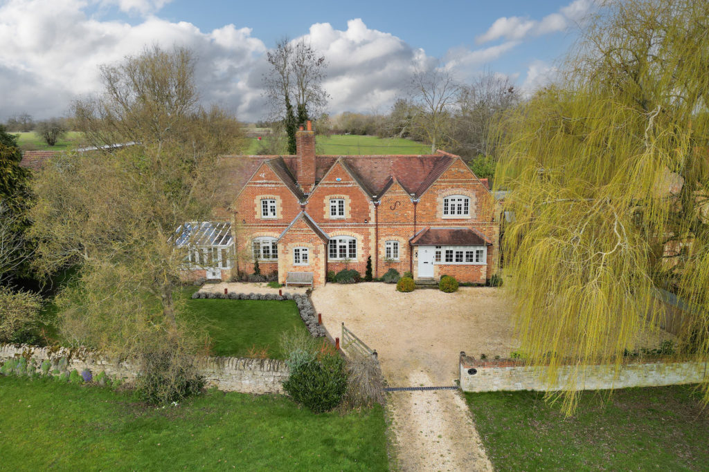 Aerial view of red brick country house with gravel driveway and willow trees.