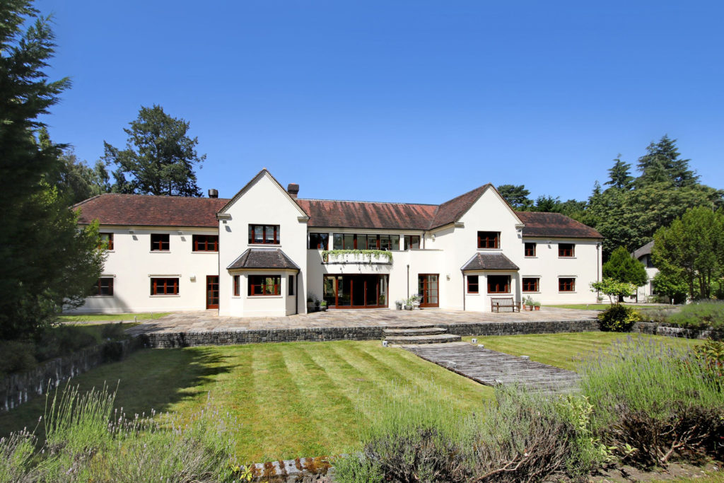 Large country house with white painted exterior, brick roof and landscaped lawns in front.