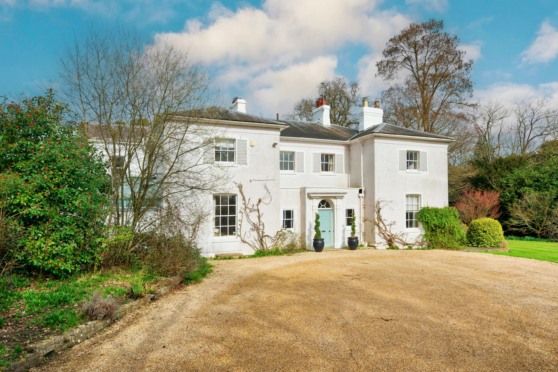 White country house with slate roof and a gravel driveway in front.