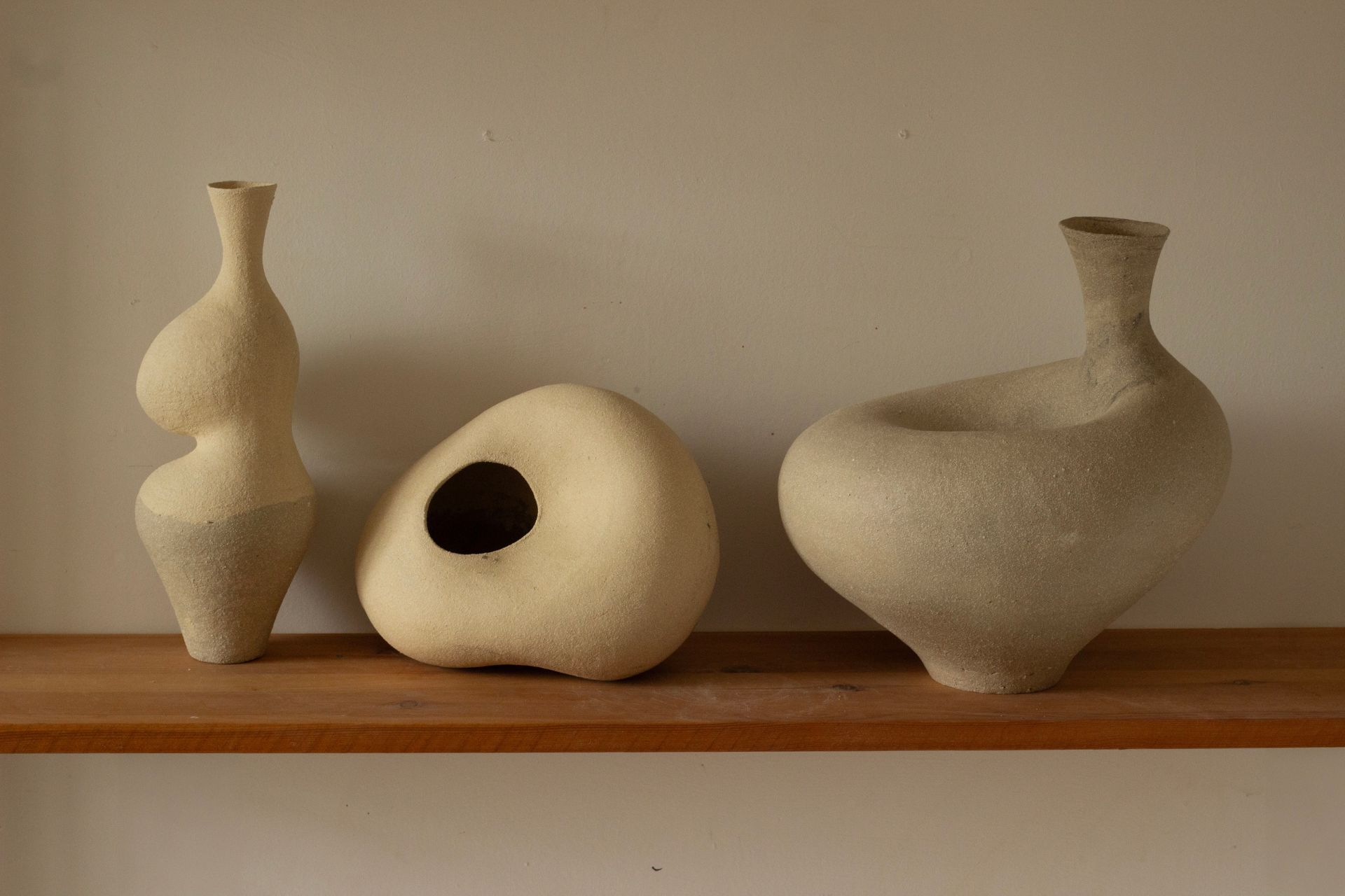 Cream vases in curved shapes, on a slim wooden shelf