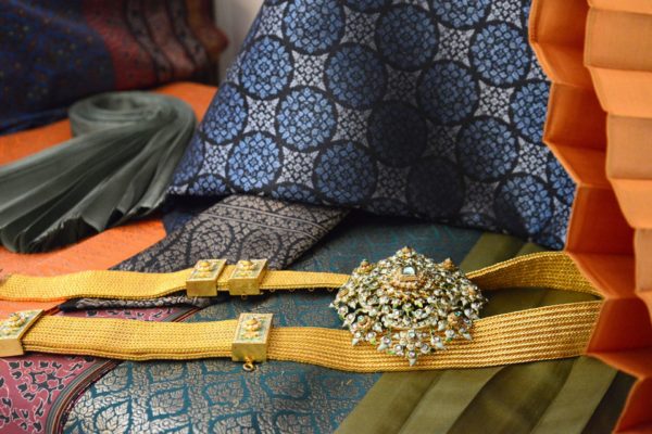 Swathes of rich patterned fabric in blue and green, with a yellow ribbon and a large sparkly brooch