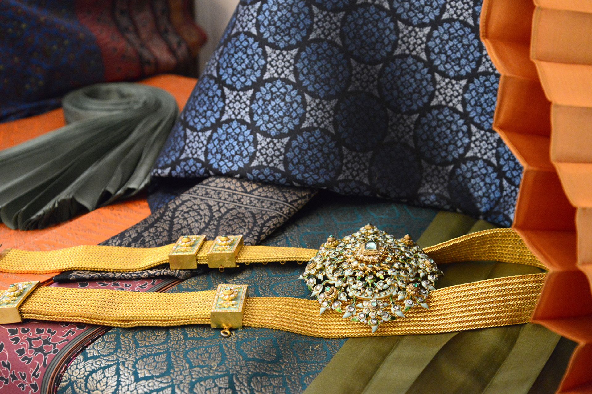 Swathes of rich patterned fabric in blue and green, with a yellow ribbon and a large sparkly brooch