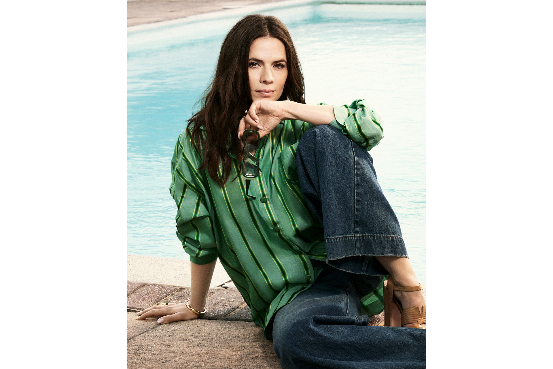 Hayley Atwell sits by a pool in a striped green shirt
