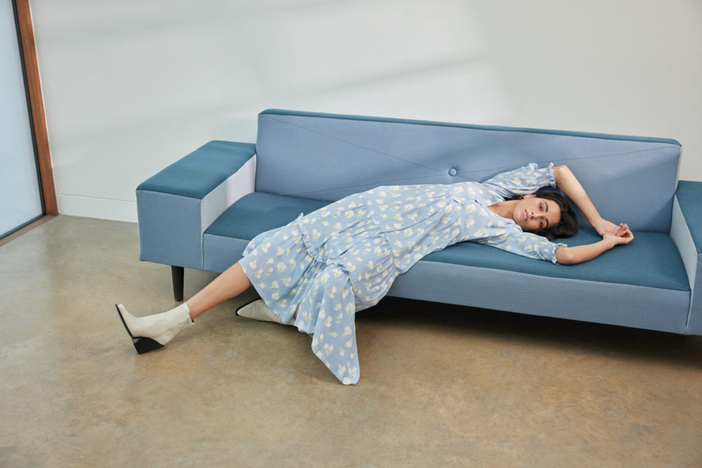 Model lies on blue sofa wearing blue floral dress from Really Wild / best British dress brands