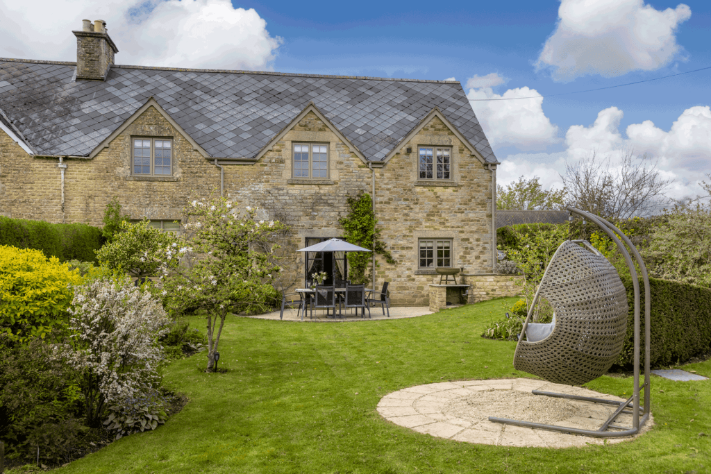 Stone cottage with shrubs surrounding and a hanging egg chair in the garden.