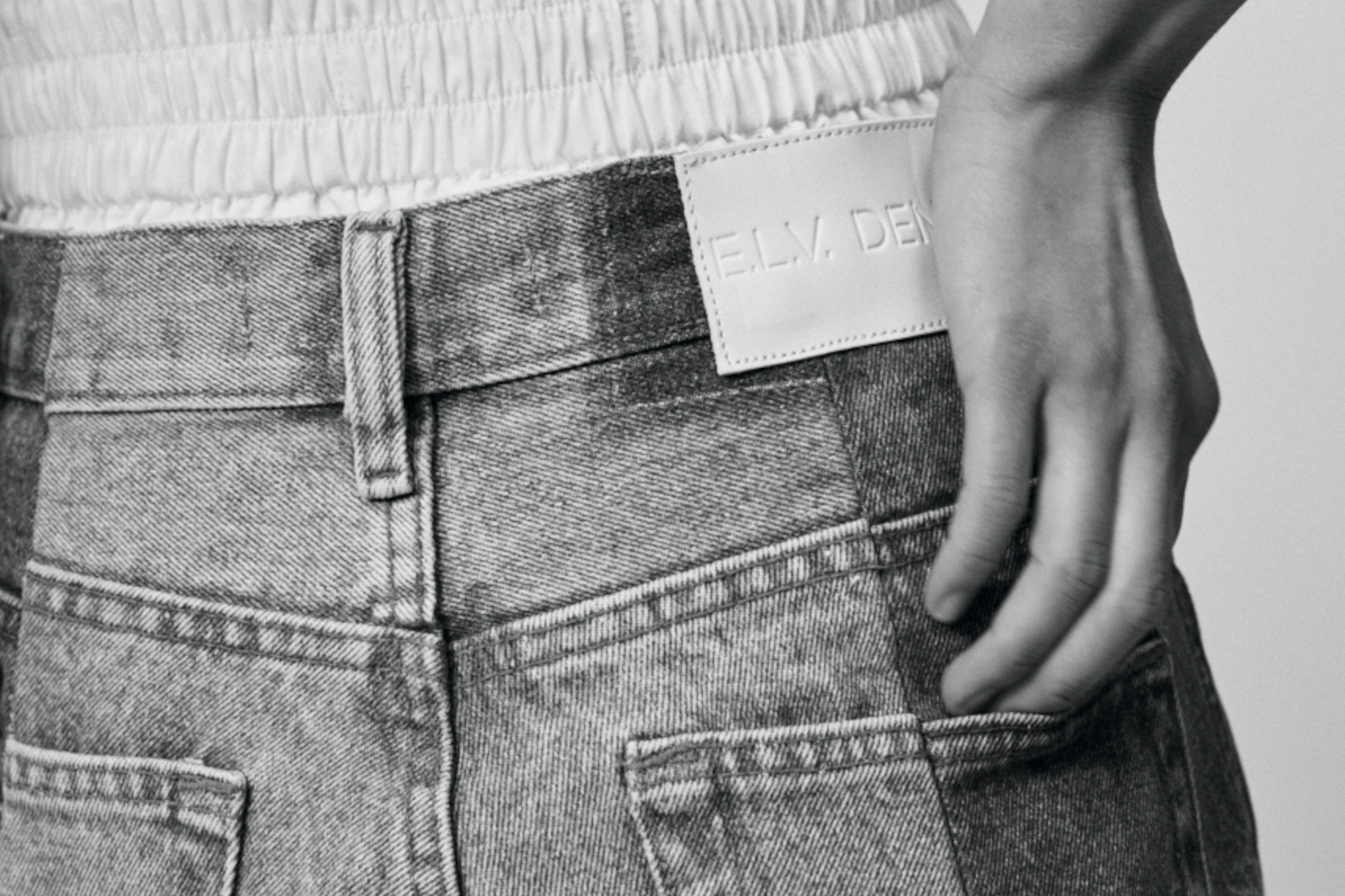 Black and white photo, close up of back of someone putting hand in jean pocket