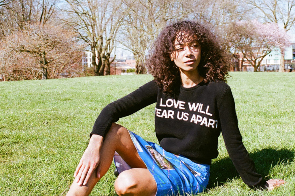 Woman sat on grass in black jumper and blue skirt