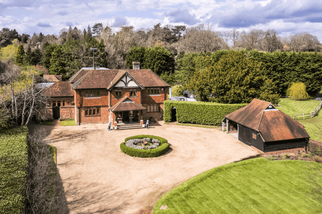 View of a large red brick home in East Sussex with a gravel driveway, red brick outbuildings and lawns surrounding.