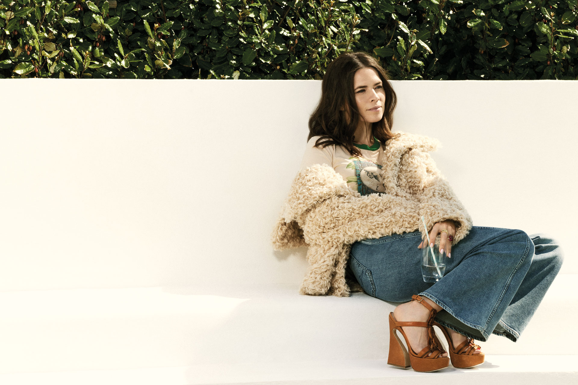 Hayley Atwell sits in a fluffy coat, blue jeans and brown strappy wedges