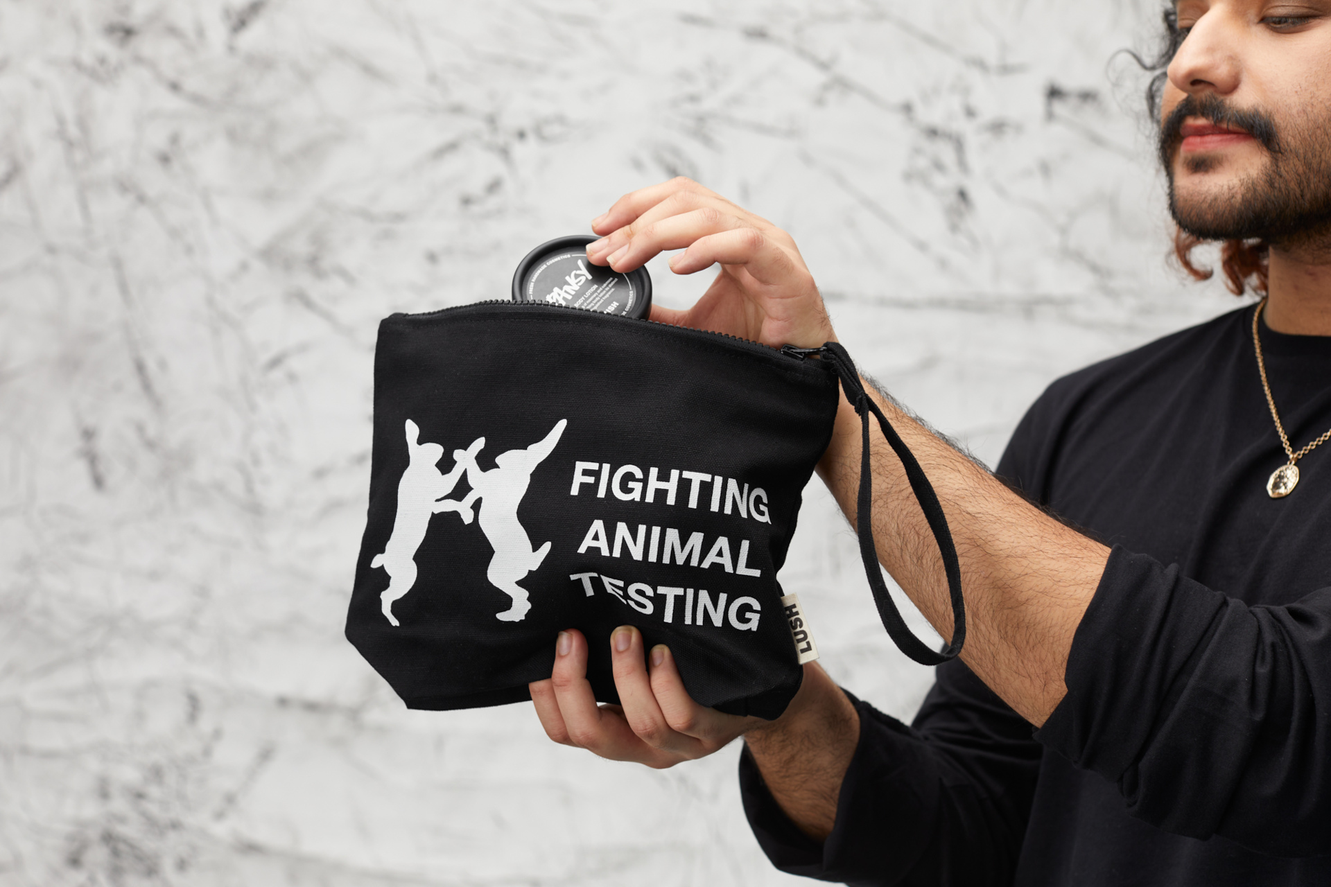 Man holding up black washbag with 'Fighting Animal Testing' on front