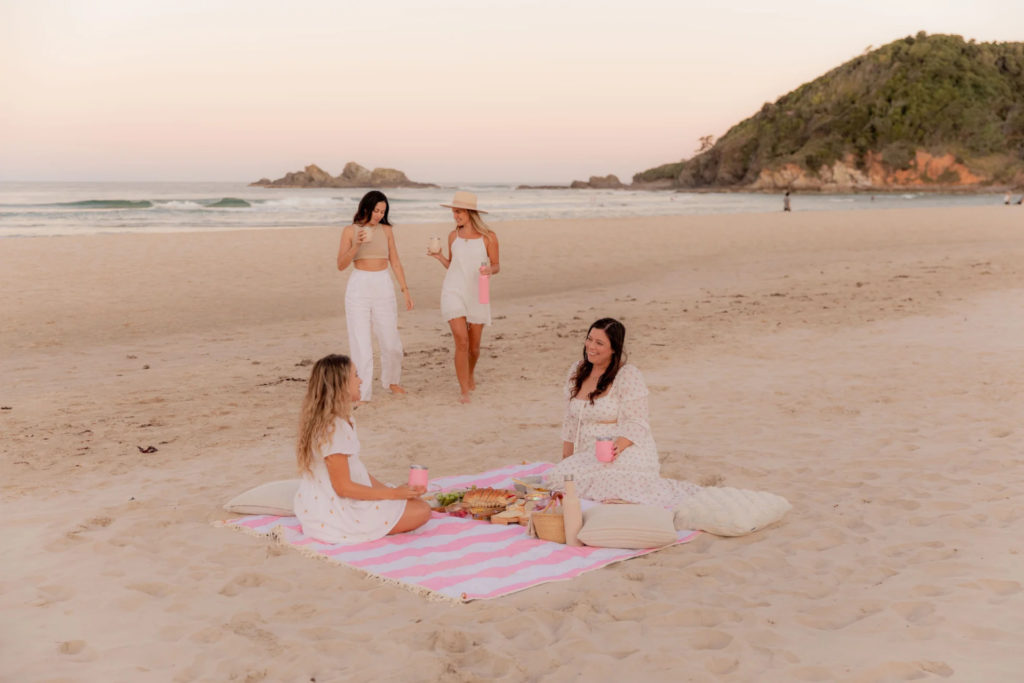 Women sat in striped pink picnic blanket on the beach