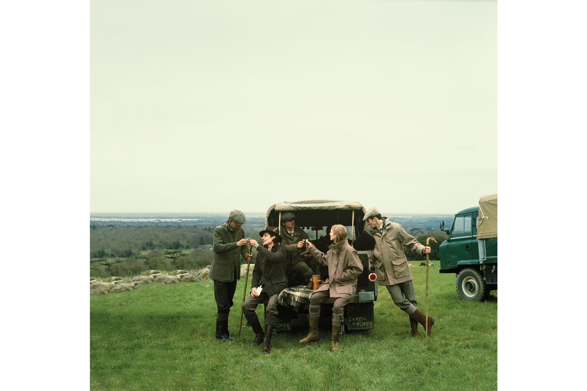 A group of people sit and stand by a 4x4 car, wearing Purdey 
