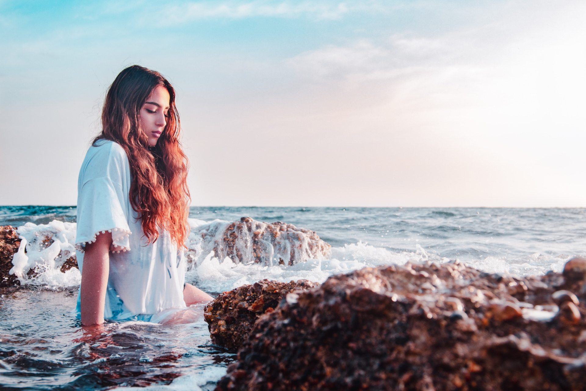 Woman sat in ocean water by rocks