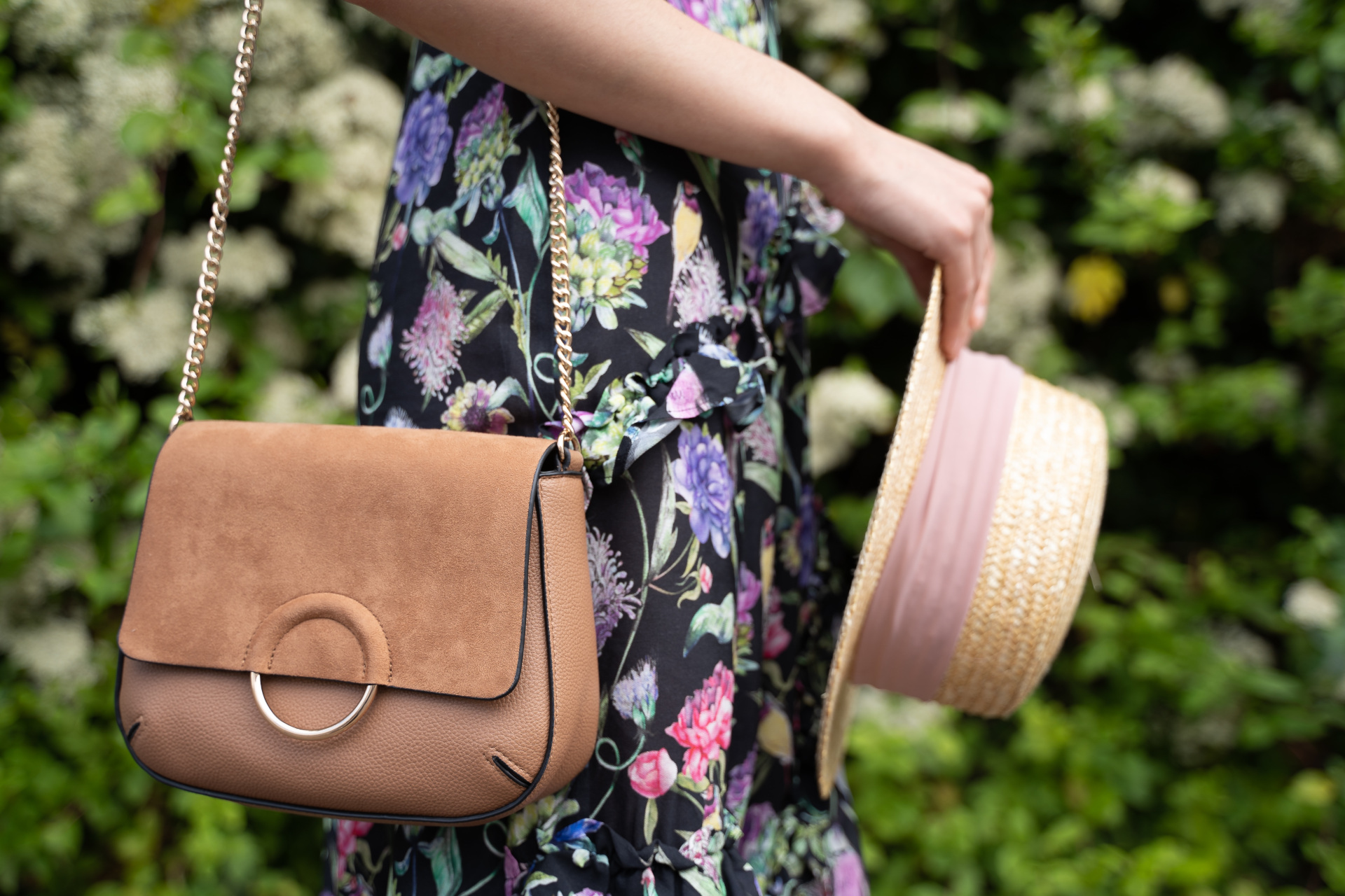 Woman in floral dress carrying brown bag and hat