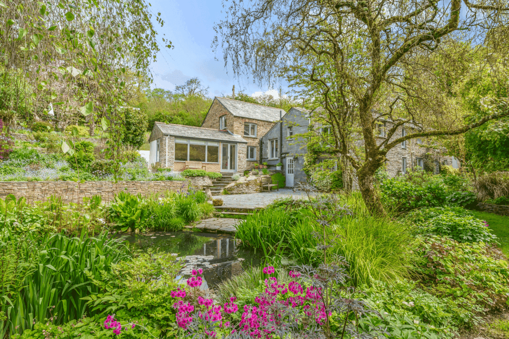 Period cottage surrounded by flowers and woodland.