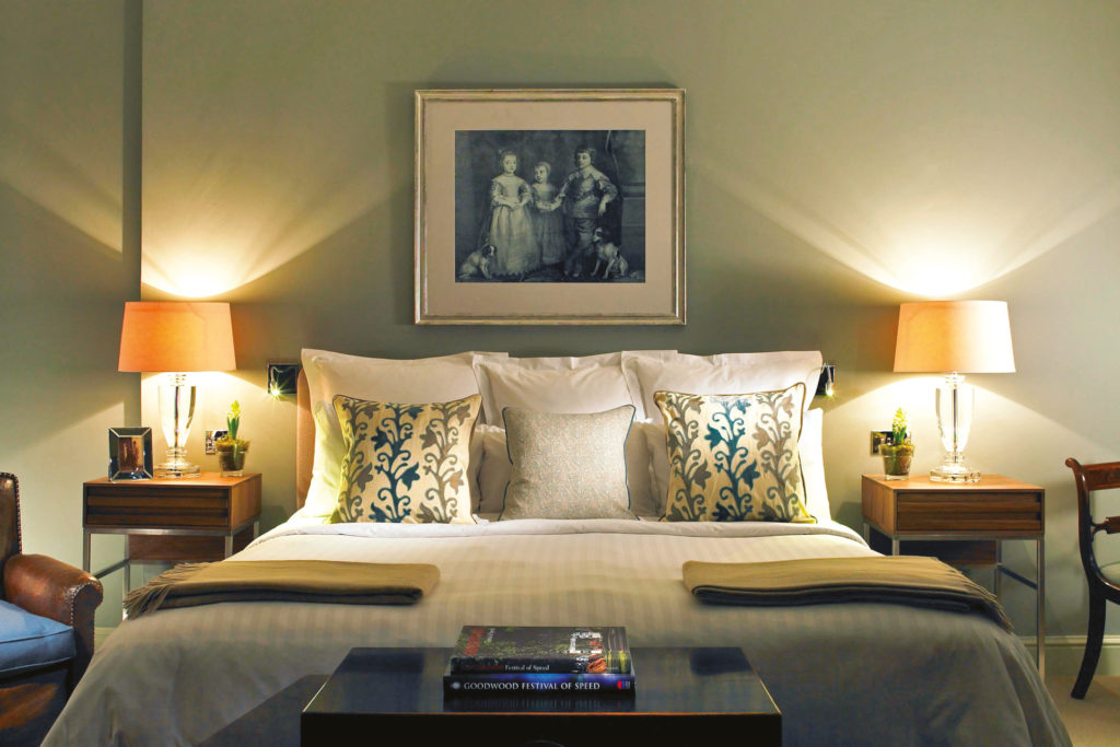 Close up of made bed with lit lamps on either side and painting on the wall above
