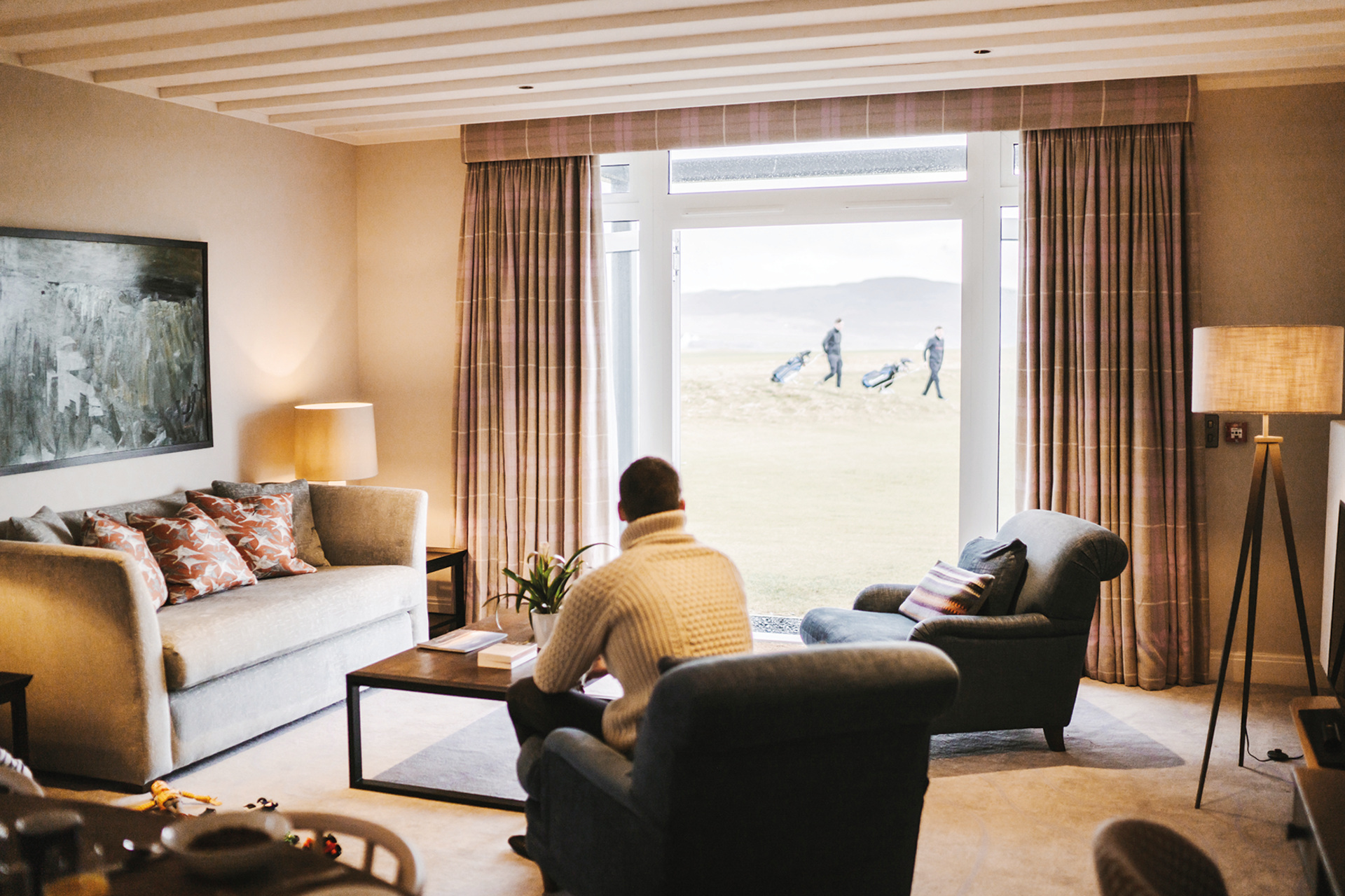 Man sat in hotel room with window look out onto people playing on golf course