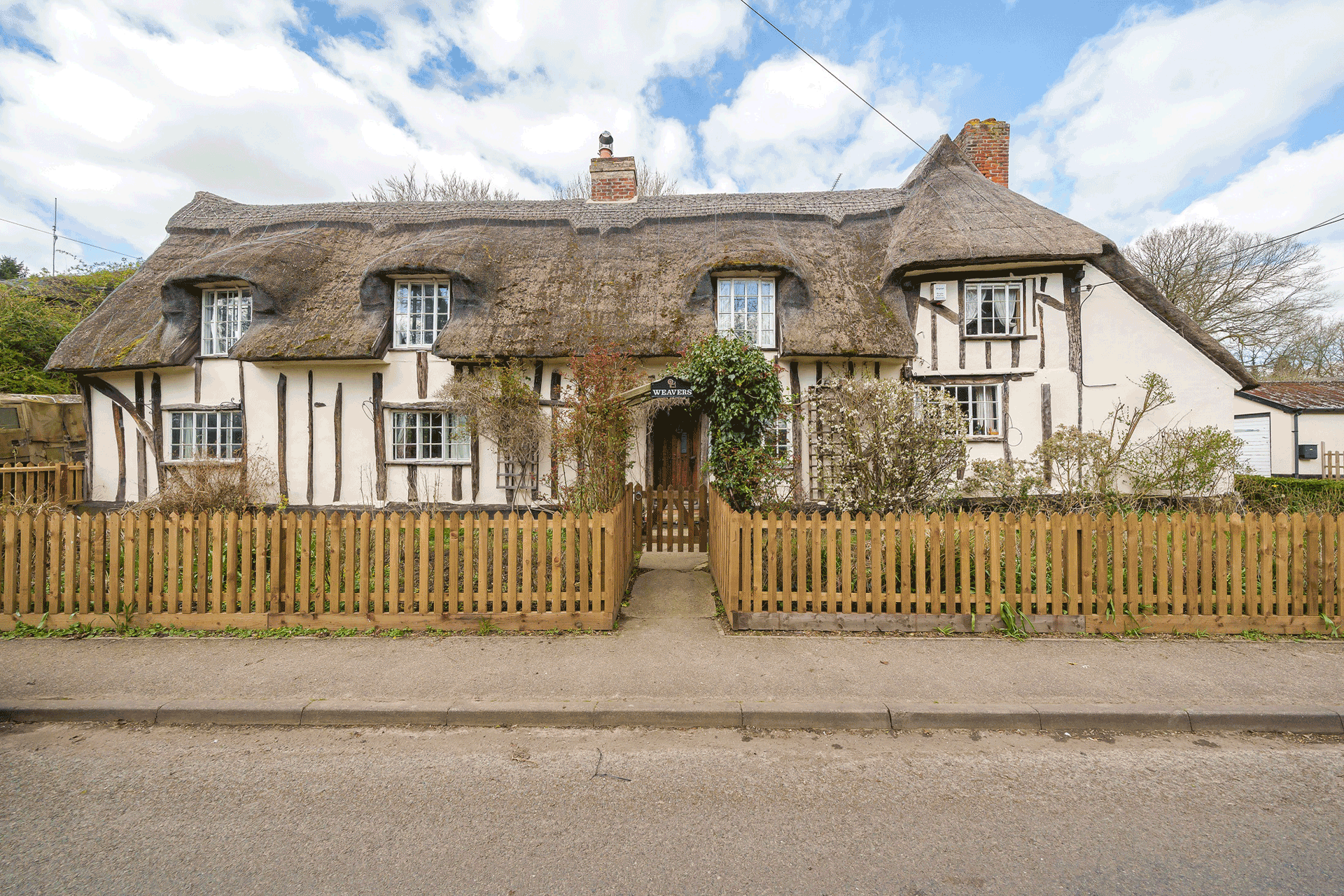 Exterior of thatched chocolate box cottage with exposed timber beams.