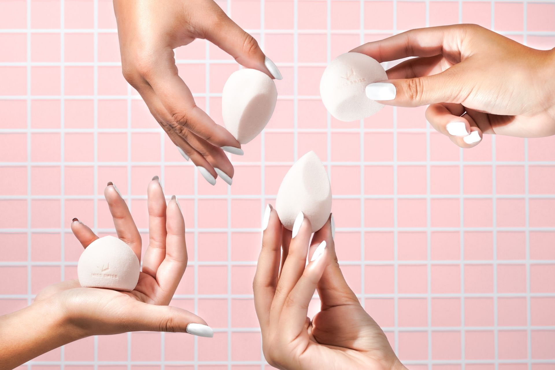 Hands holding beauty blender in front of pink tile background