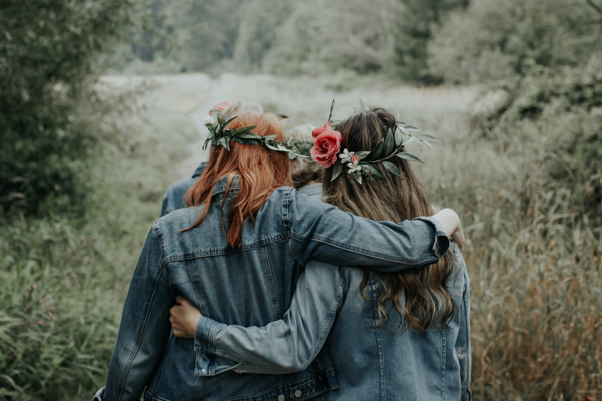 Two women wearing flowers crowns hugging in a field