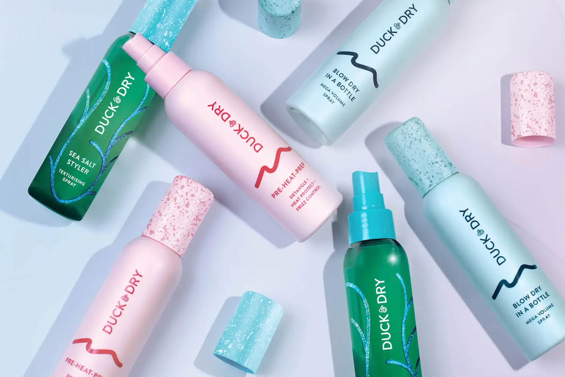 Pink. blue and dark green bottles of dry shampoo against a pale blue background.