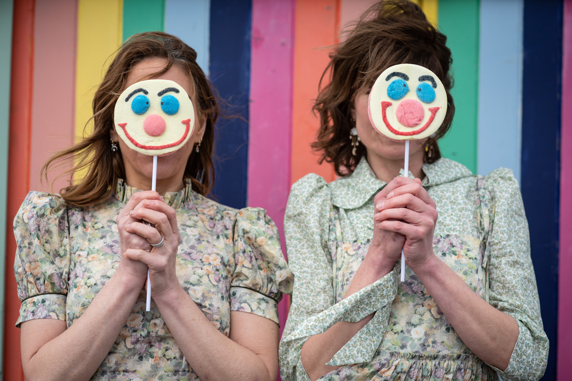 Woman stood in front of rainbow boards with smiley face lollies held over their faces