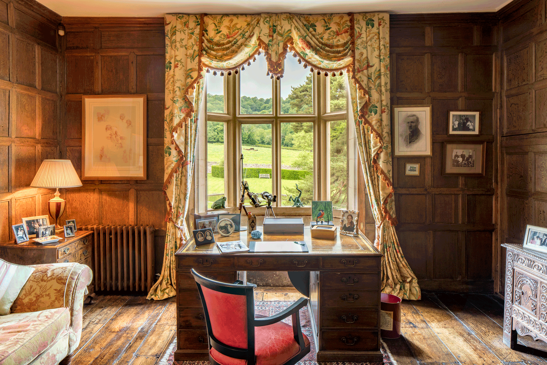 Study with wood-panelled walls, a mahogany desk and a red chair.