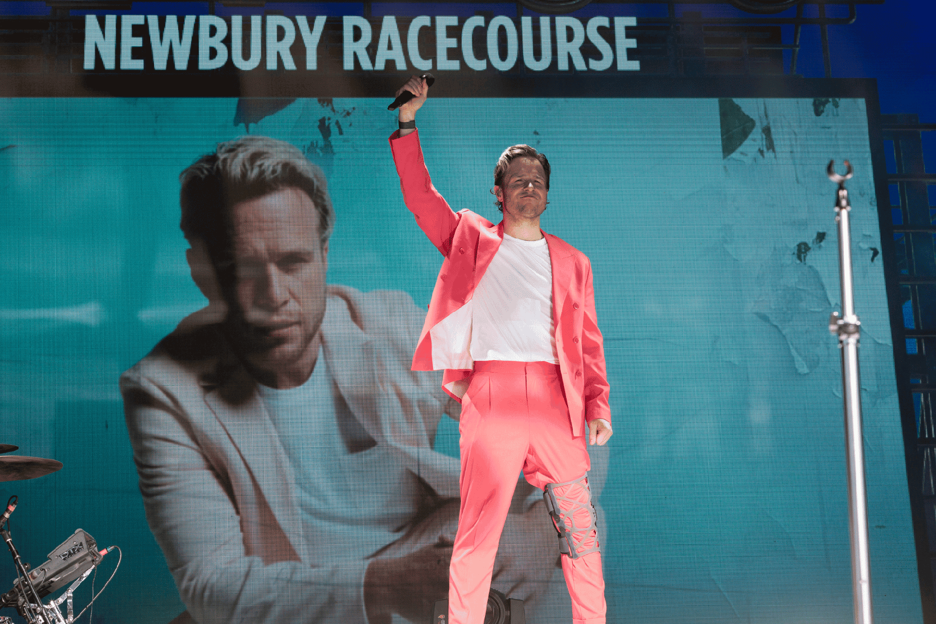 Olly Murs on stage at Newbury Racecourse wearing a coral pink suit.