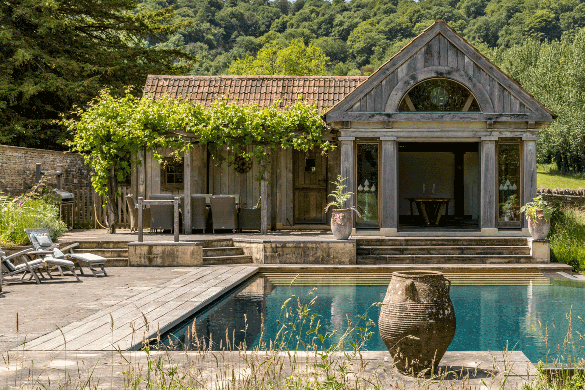 Romanesque pool house with pool in front and shrubs surrounding.