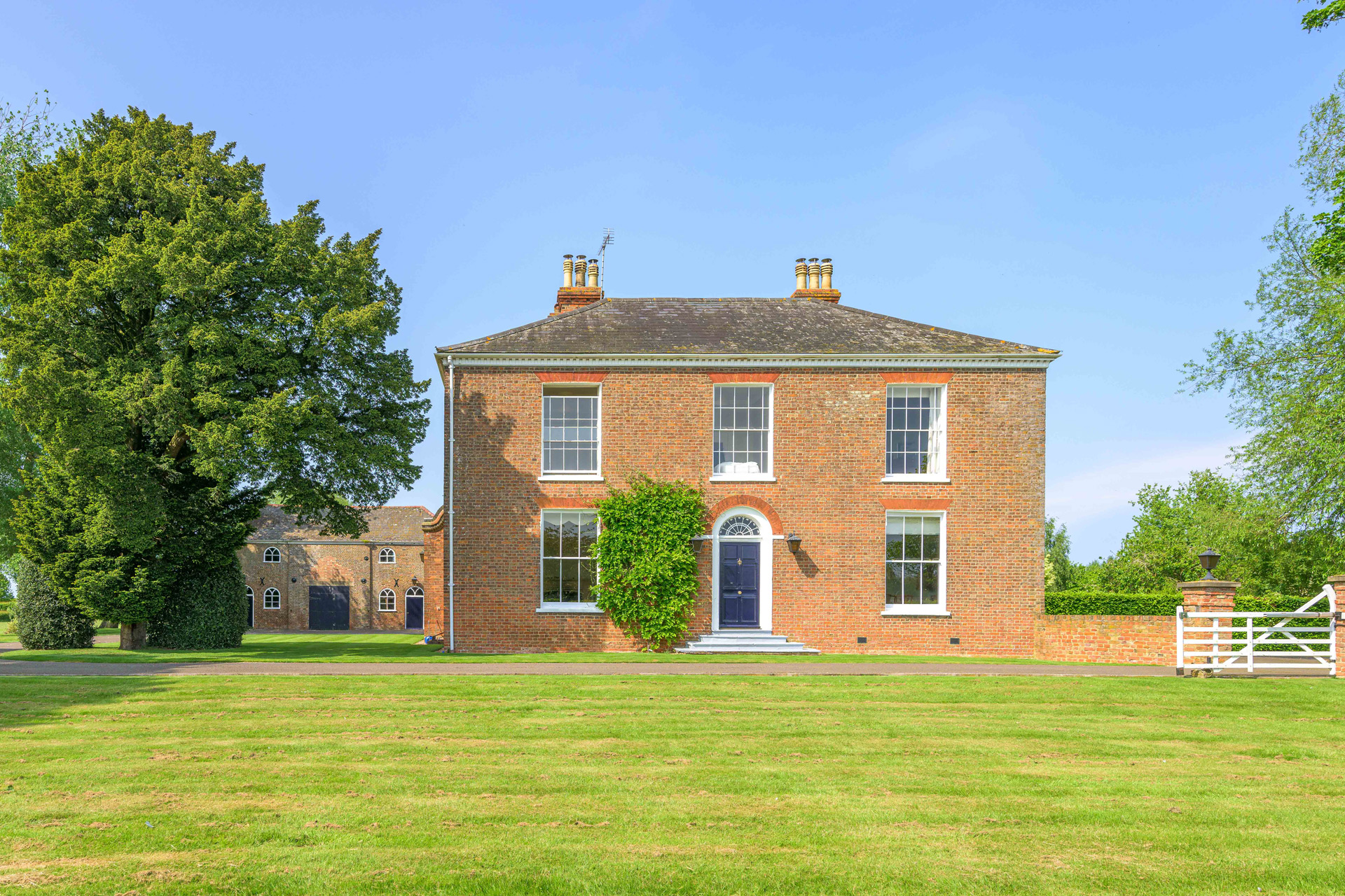 Large red brick country house with arched doorway and a lawn in front.