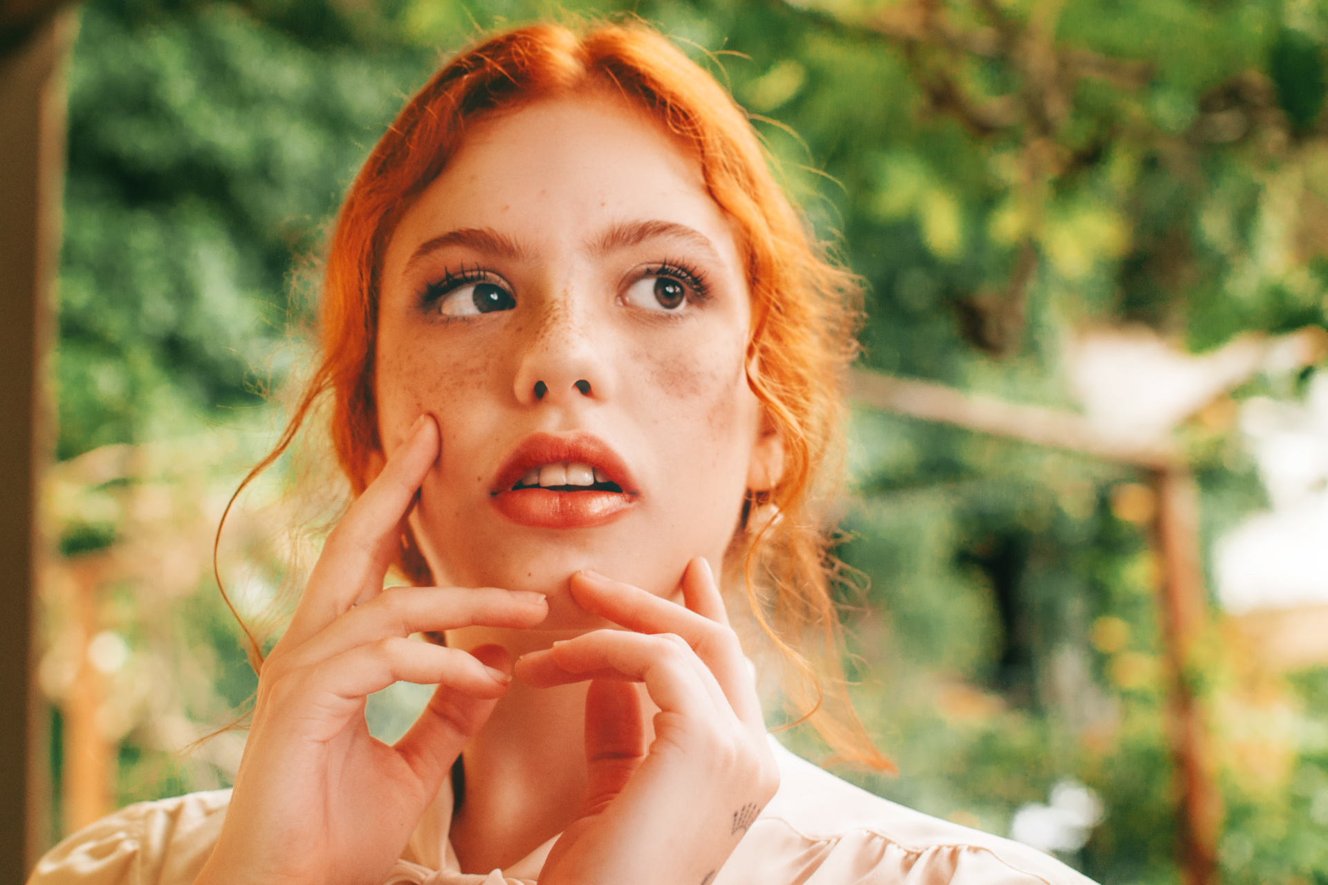 Woman with red hair looking up with hands on her face