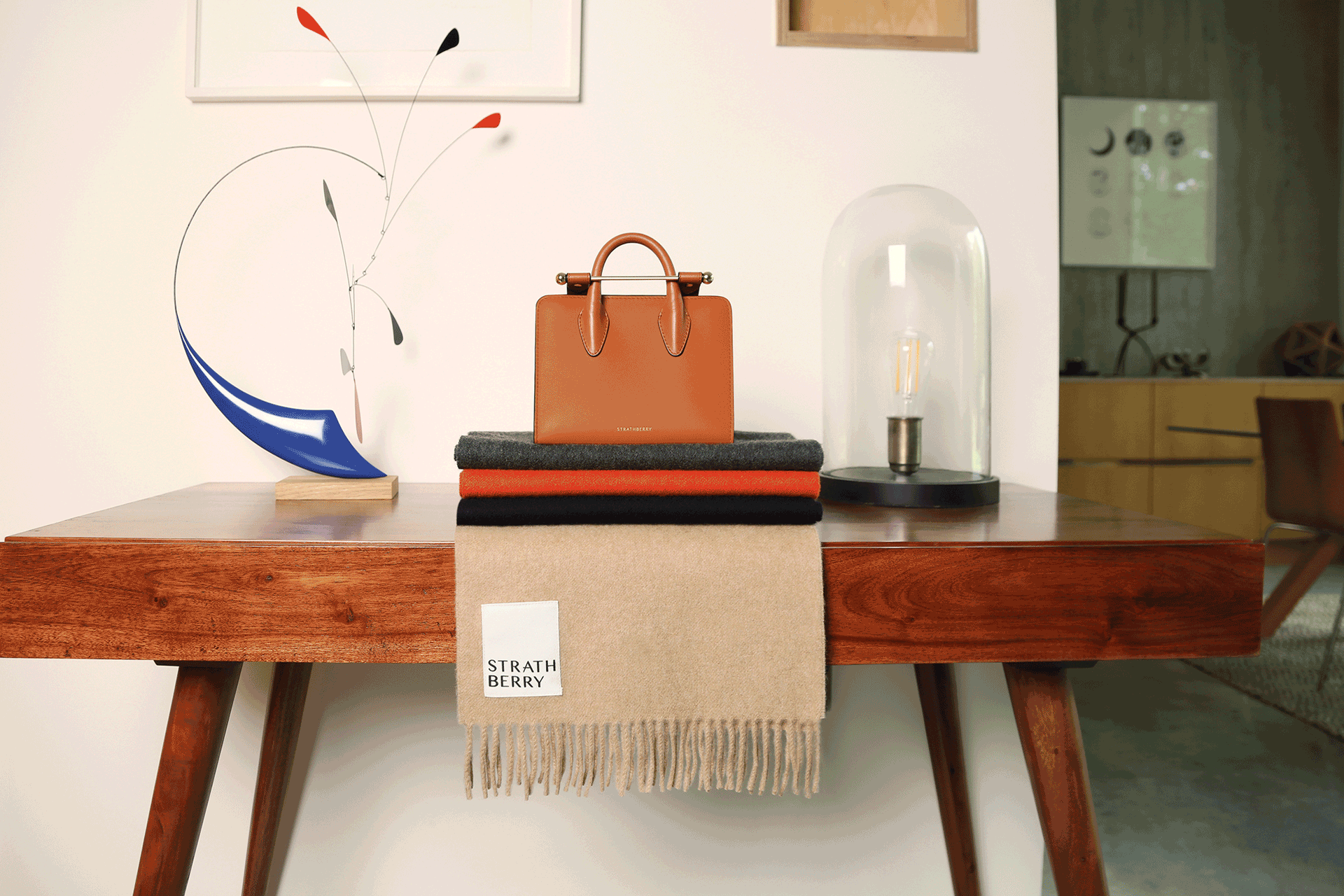 Strathberry Nano tote in chestnut sitting on top of folded cashmere scarves.